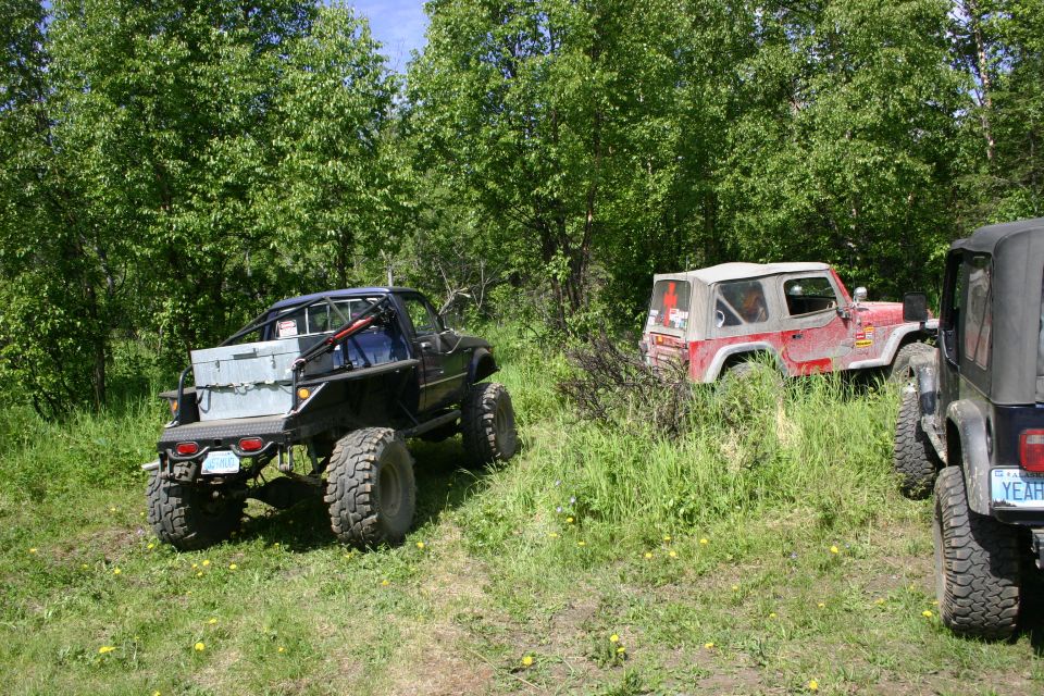 Black Jeep Wrangler with large tires and a toolbox in the bed, parked on a grassy field