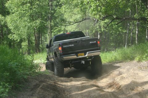 2003 Jeep TJ - A black Dodge Ram pickup truck navigates a dusty trail through a wooded area.