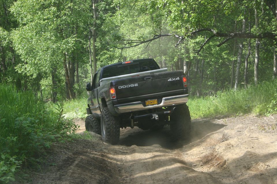 Black Dodge Ram pickup truck with 4x4 badging driving on a dirt trail, kicking up dust