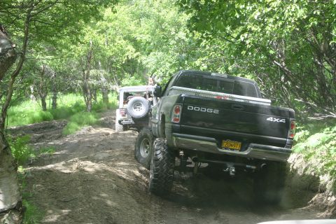 2003 Jeep TJ - A black Dodge Ram pickup truck and a Jeep Wrangler navigate a muddy off-road trail.