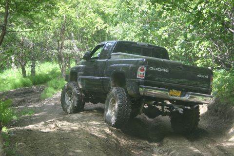 2003 Jeep TJ - A lifted black Dodge pickup truck navigates a muddy off-road trail.