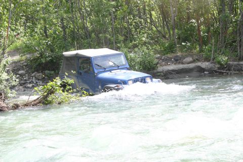 2003 Jeep TJ - A blue Jeep Wrangler navigates a fast-flowing river surrounded by trees.