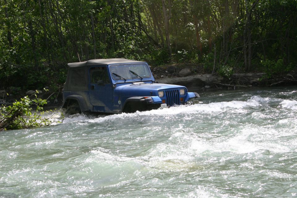 Blue Jeep Wrangler driving through river rapids