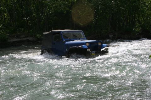 2003 Jeep TJ - A blue Jeep Wrangler navigates a rocky riverbed, its tires churning through the white water.
