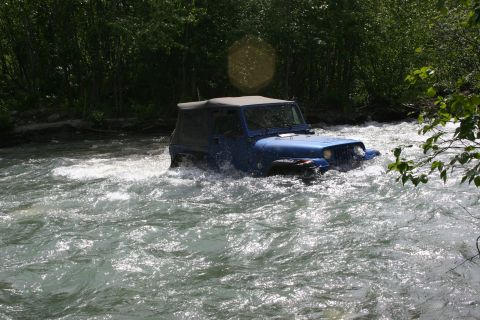 2003 Jeep TJ - A blue 2003 Jeep Wrangler navigates through a fast-flowing river surrounded by trees.