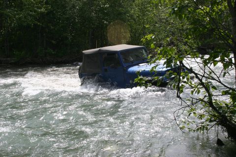 2003 Jeep TJ - Blue 2003 Jeep TJ navigates a rocky river, water splashing around its tires.