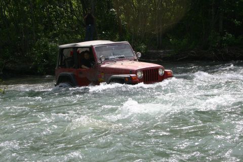 2003 Jeep TJ - A red 2003 Jeep TJ navigates a rocky river crossing with trees in the background.