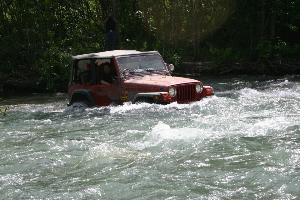 Red 2003 Jeep TJ driving through a river, water splashing around it