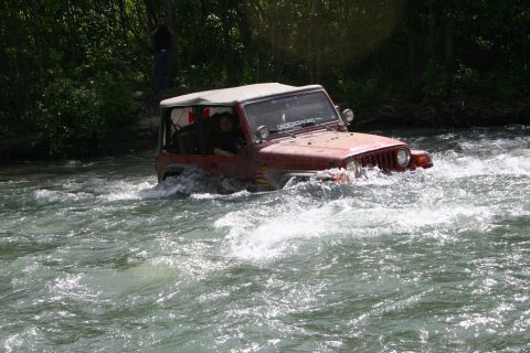 2003 Jeep TJ - A red Jeep Wrangler navigates through a fast-moving river, with trees and a person visible on the bank.