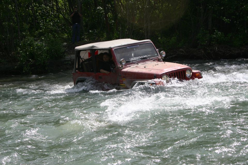 red Jeep Wrangler driving through a river, has a sticker on windshield that says UNDERGROUND
