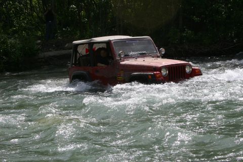 2003 Jeep TJ - A red Jeep Wrangler navigates a fast-flowing river, its tires submerged in the turbulent water.