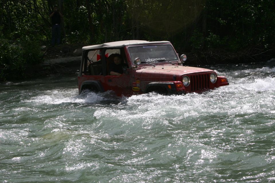 Red Jeep Wrangler driving through a river, with "UNDERGROUND" sticker on windshield