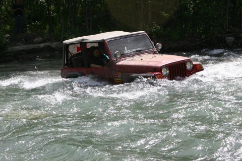 2003 Jeep TJ - A red 2003 Jeep TJ navigates a rocky river, its soft top visible as it splashes through the water.