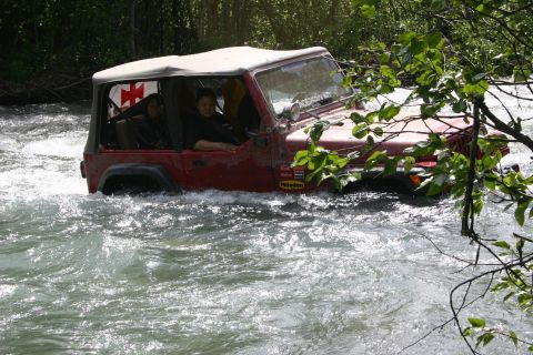 2003 Jeep TJ - A red Jeep Wrangler navigates a fast-flowing river, with trees and foliage on the banks.