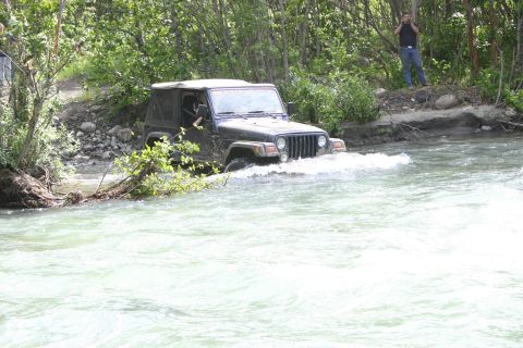 2003 Jeep TJ - A Jeep Wrangler navigates a shallow river surrounded by trees.