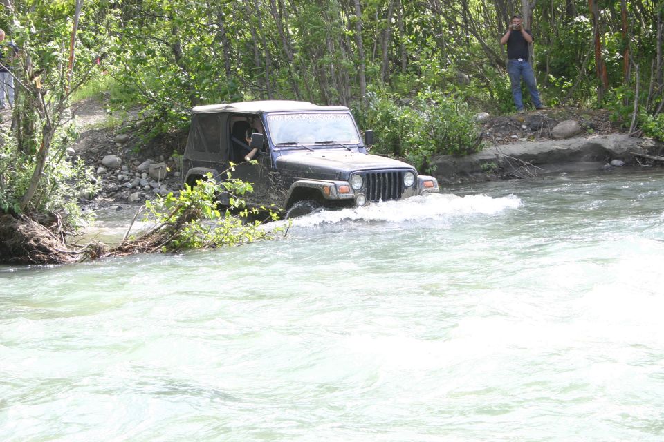 Dark gray Jeep Wrangler driving through a river, front 3/4 view