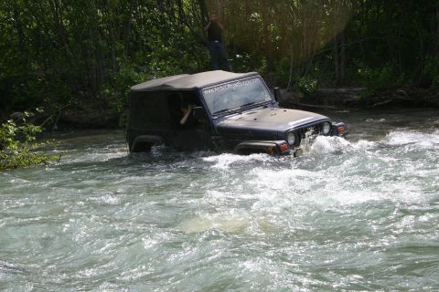 2003 Jeep TJ - A Jeep TJ navigates a rocky river, kicking up water as it goes.