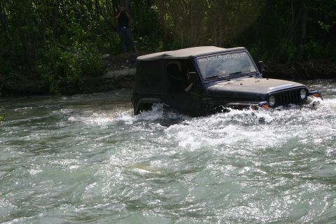 2003 Jeep TJ - A dark blue Jeep Wrangler navigates through a flowing river, with a person visible in the background.