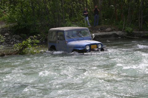 2003 Jeep TJ - A blue 2003 Jeep TJ navigates a rocky riverbed, with two people observing from the bank.