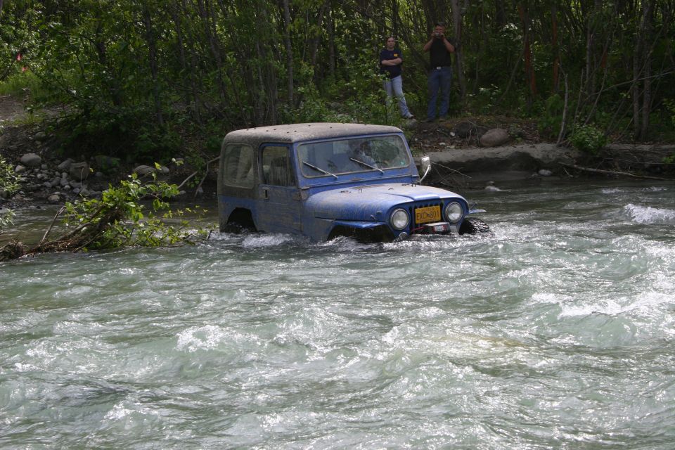 Blue 2003 Jeep TJ driving through a fast-flowing river, front 3/4 view