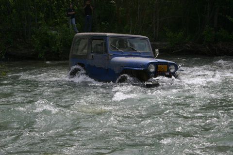 2003 Jeep TJ - Blue Jeep Wrangler navigates a fast-flowing river with trees on the bank.