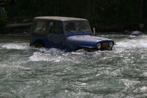 2003 Jeep TJ - A blue Jeep Wrangler navigates a fast-moving river, with water reaching its doors.
