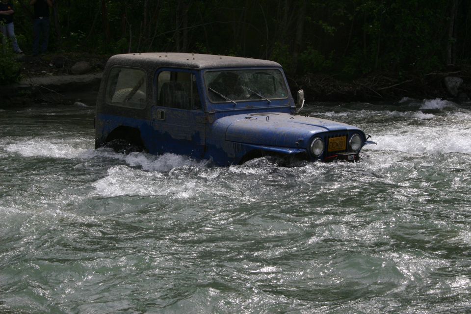 blue Jeep Wrangler driving through river, water up to its doors
