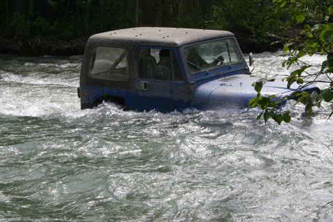 2003 Jeep TJ - A blue Jeep Wrangler navigates through a fast-moving river, partially submerged.