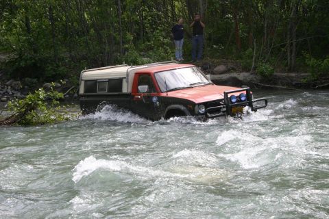 2003 Jeep TJ - A pickup truck navigates a fast-moving river, with two people watching from the bank.