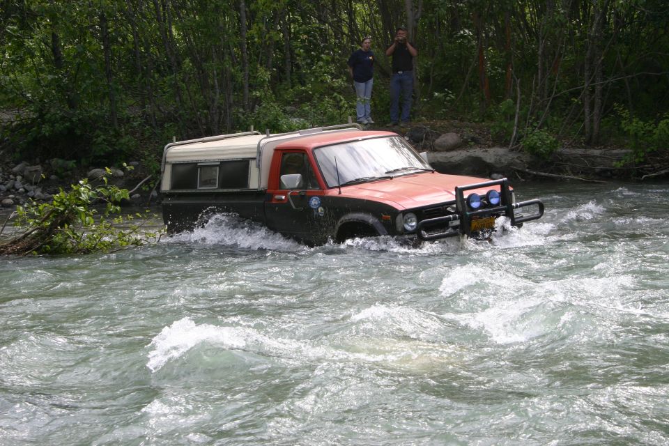 red and black pickup truck with a camper shell driving through a river