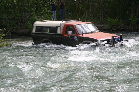 2003 Jeep TJ - A pickup truck navigates a fast-flowing river, with two people watching from the bank.