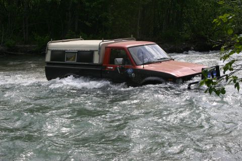 2003 Jeep TJ - Pickup truck navigates through a fast-moving river with trees in the background.