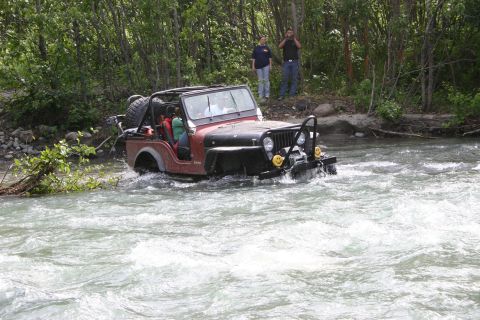 2003 Jeep TJ - A red Jeep Wrangler navigates a river, with two people watching from the bank.