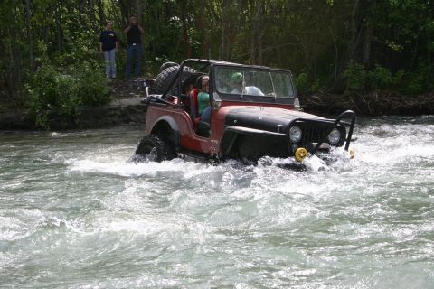 2003 Jeep TJ - Jeep CJ navigates a fast-flowing river, with two passengers visible inside.