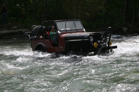 2003 Jeep TJ - A red Jeep CJ navigates through a fast-flowing river surrounded by trees.