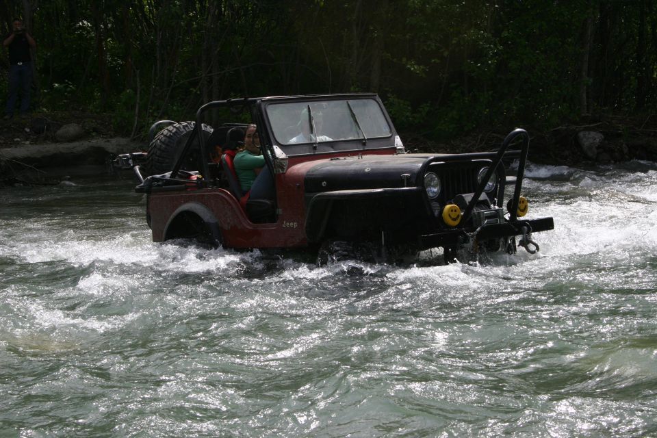 Jeep CJ driving through a river, people inside. It has a winch and brush guard