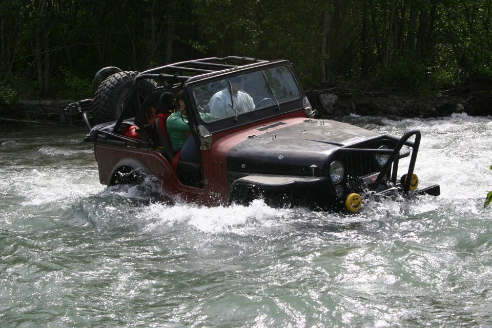 Red and black Jeep Wrangler driving through a river, with a spare tire on the back and a roll cage