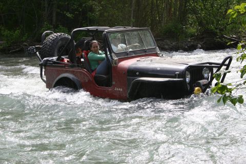 2003 Jeep TJ - A red and black Jeep navigates through a fast-moving river, with two people inside.