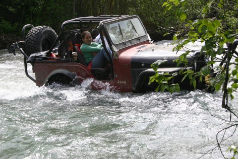 2003 Jeep TJ - Jeep Wrangler navigates a rocky riverbed, kicking up spray.