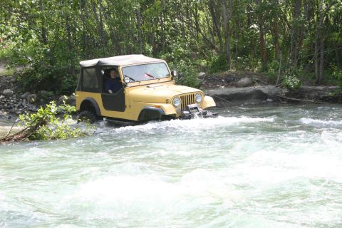 2003 Jeep TJ - A yellow Jeep Wrangler navigates a rocky river, its body style suggesting it is a CJ model from the 1980s, not a 2003 model.