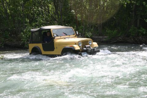 2003 Jeep TJ - Yellow Jeep CJ navigates a rocky riverbed with trees in the background.