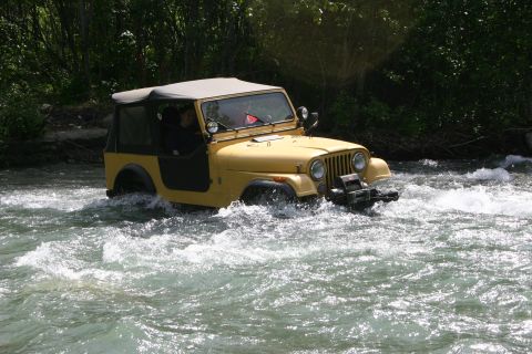 2003 Jeep TJ - A yellow Jeep CJ-7 navigates through a rocky river with trees in the background.