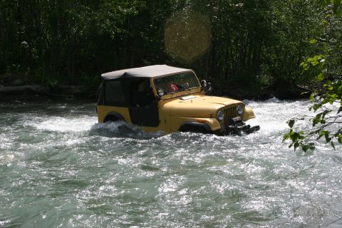 2003 Jeep TJ - Yellow Jeep CJ navigates a fast-flowing river with trees in the background.