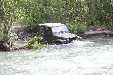 2003 Jeep TJ - A Jeep Wrangler navigates a shallow river, kicking up water as it moves through the natural obstacle.