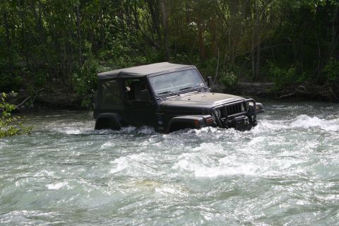 2003 Jeep TJ - A dark-colored 2003 Jeep TJ navigates a fast-flowing river surrounded by trees.
