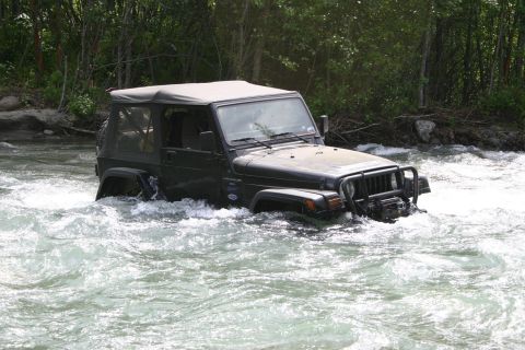 2003 Jeep TJ - A Jeep Wrangler navigates through fast-moving river water surrounded by trees.
