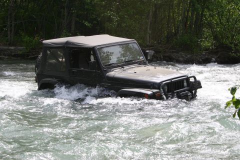 2003 Jeep TJ - A Jeep Wrangler navigates a fast-flowing river surrounded by trees.