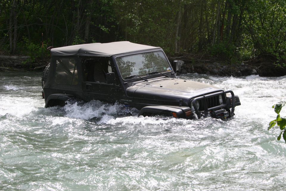 Dark green Jeep Wrangler driving through a river, front bumper visible