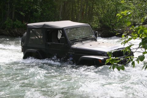 2003 Jeep TJ - A black 2003 Jeep Wrangler navigates through a fast-flowing river surrounded by trees.