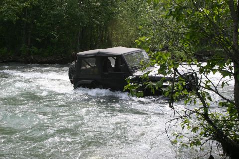 2003 Jeep TJ - Jeep TJ navigates a river, surrounded by lush green foliage.